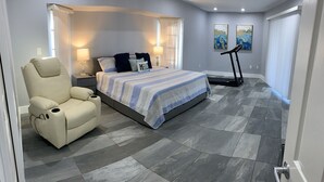 Un dormitorio con cama, sillón de masaje, cinta de correr y obras de arte en las paredes.