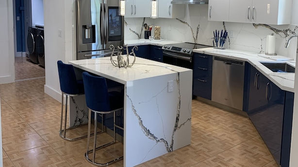 Una cocina moderna con una isla de mármol, electrodomésticos de acero inoxidable y taburetes de bar azules.