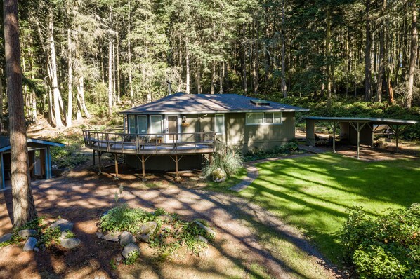 A cabin with a deck, surrounded by a forest. - TreeTops Forest Retreat (Lopez Island)