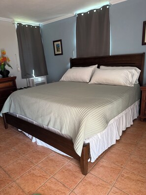 A bedroom with a wooden bed, a nightstand, a bedside table, a wall-mounted air conditioner, and a framed picture. - Oceanview Lighthouse Villa (Maunabo)