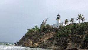 Um farol numa falésia rochosa, com ondas quebrando abaixo.
