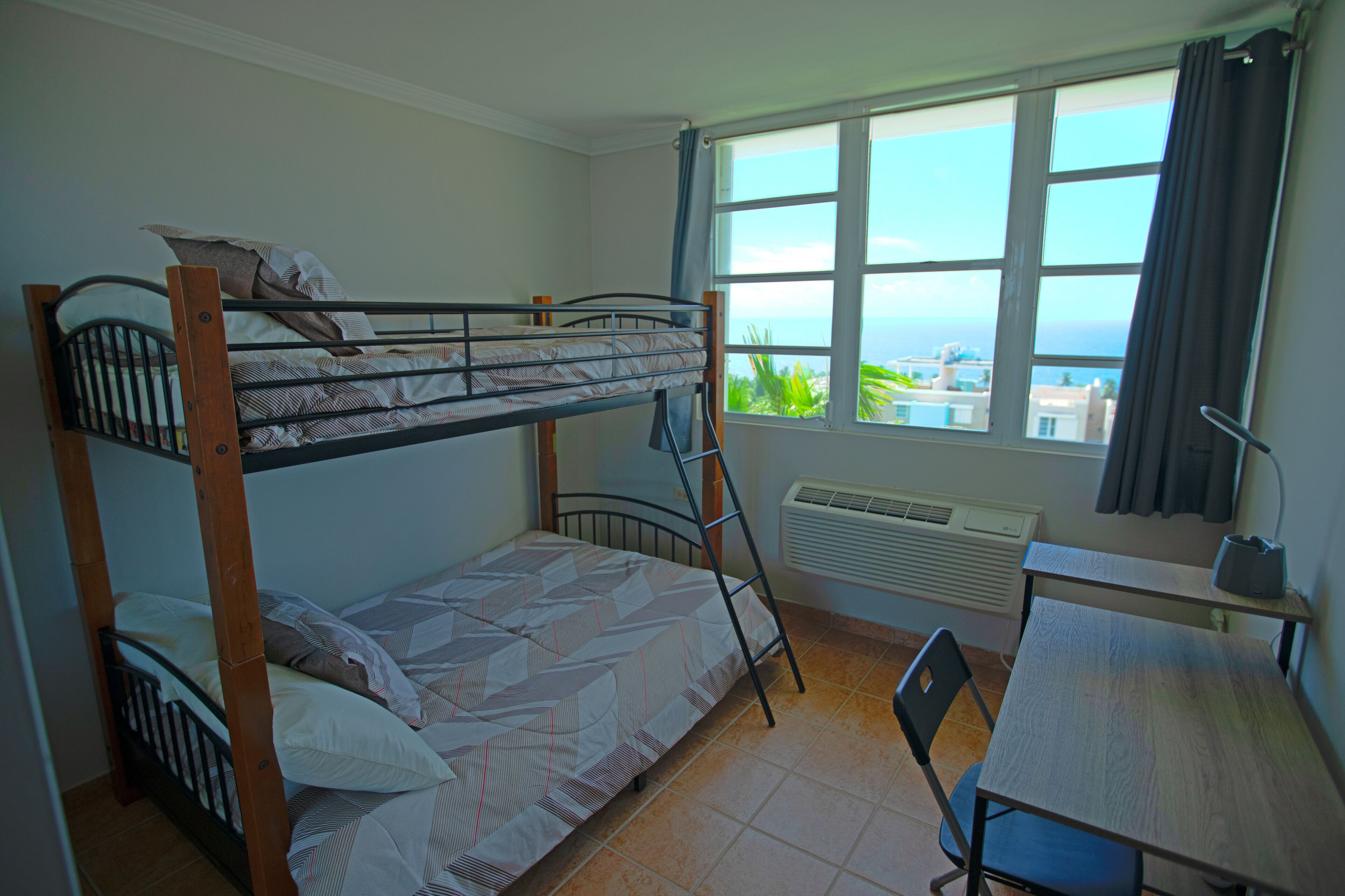 A bunk bed room with a view of the sea, a desk, and a chair.