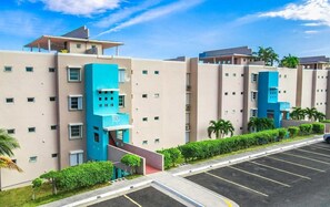 A multi-story hotel with a parking lot, a blue accent building, and palm trees. - Oceanview Lighthouse Villa (Maunabo)