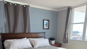 A neatly made bed with a wooden headboard, a bedside table with a plant, and a window with curtains.