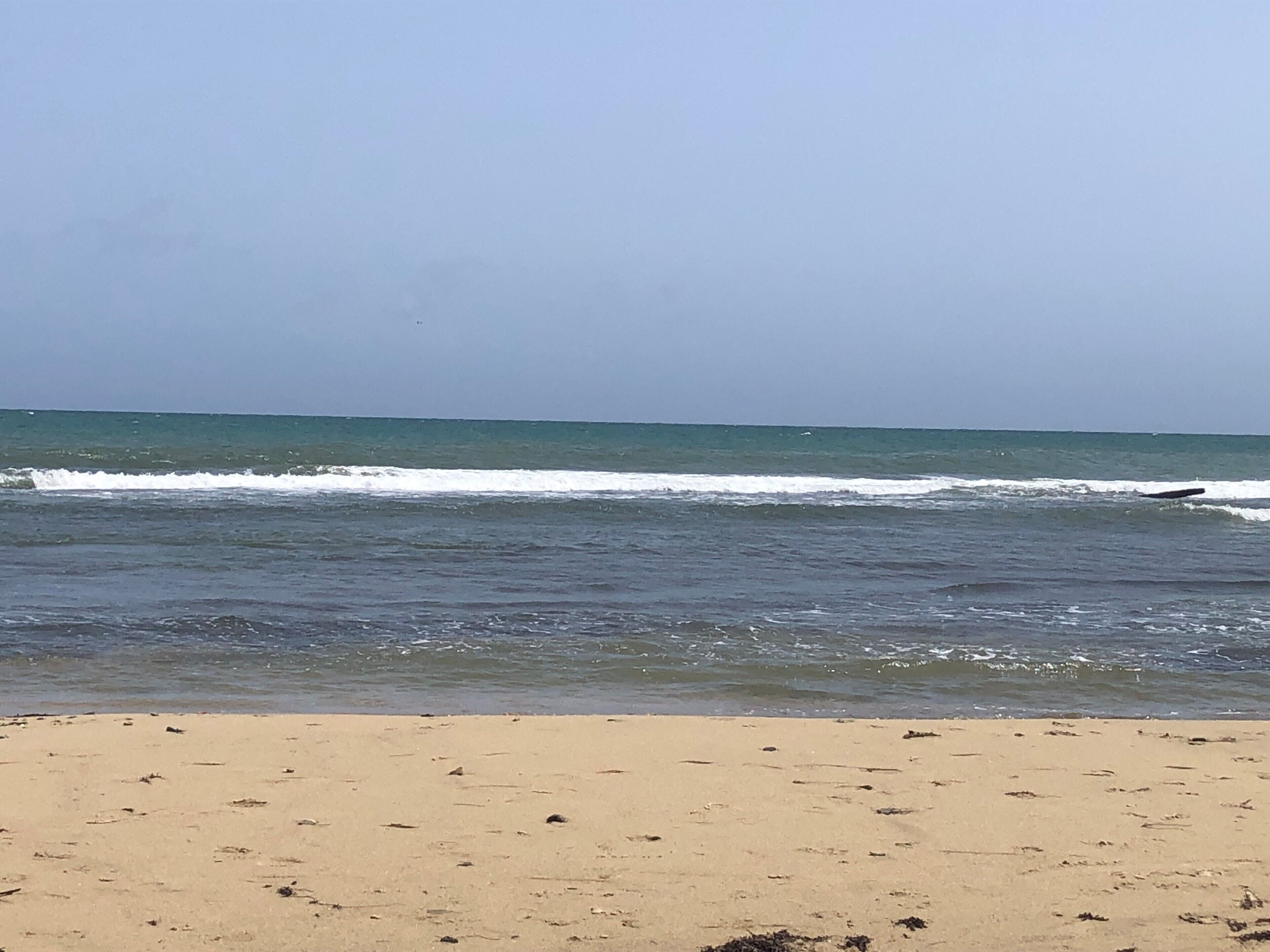 Een strand met golven, een heldere lucht en een zandstrand.