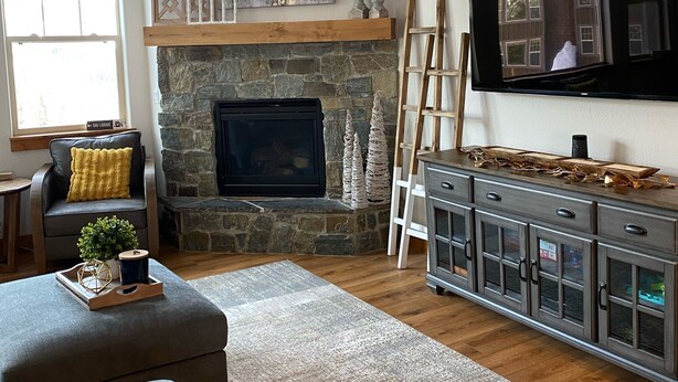 A living room with a stone fireplace, a television mounted on the wall, and a large window. - Updated Schweitzer condo with beautiful mountain and valley views!  (Sandpoint)