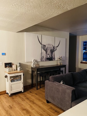 Una sala de estar con estación de café, un sofá, una mesa de comedor y un cuadro de toro en la pared.