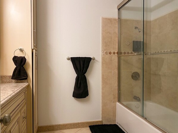 Ein Badezimmer mit Duschkabine aus Glas, einem Handtuchhalter mit schwarzem Handtuch und einer Marmorplatte.