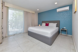 Una camera d'albergo moderna con un letto grande, un comodino, un condizionatore d'aria e una finestra con tende leggere.