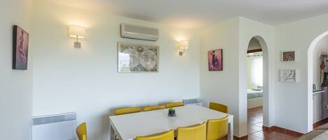 A dining area with a white table and yellow chairs, a world map on the wall, and a small plant on the table.