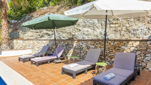 A poolside area with lounge chairs and umbrellas, a stone wall, and a tiled floor. - Villa Flamenca Canillas de Albaida by Ruralidays (Málaga)