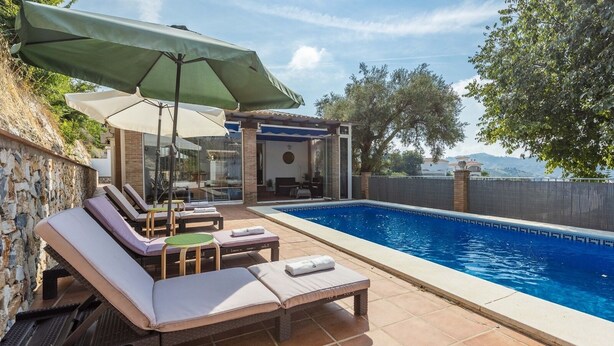 A swimming pool with lounge chairs and umbrellas, a stone wall, and a view of the landscape. - Villa Flamenca Canillas de Albaida by Ruralidays (Málaga)