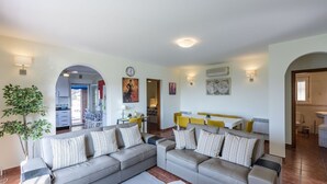 A living room with a grey sofa set, a dining area with yellow chairs, and a kitchen visible through an archway. - Villa Flamenca Canillas de Albaida by Ruralidays (Málaga)