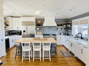 A modern kitchen with white cabinetry, a central island with bar stools, a stainless steel refrigerator, a microwave, and a stove.
