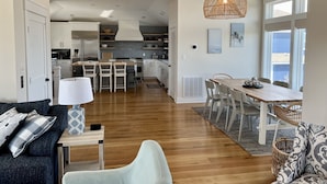 A spacious living area with a dining table, a sofa, and a kitchen in the background. - Great for Families, Salt Water Pool, Sea & Sound Views, Quiet Gated Cul-De-Sac (Kitty Hawk)