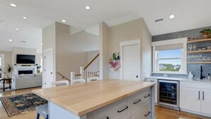 A modern kitchen with a central island, white cabinetry, and a view of the outdoors. - Great for Families, Salt Water Pool, Sea & Sound Views, Quiet Gated Cul-De-Sac (Kitty Hawk)