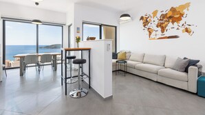 A modern living room with a large window, a sofa, a coffee table, and a map on the wall. - Modern Top Floor Sea View 3BR-Pool Spa Gym Luxury (Becici)