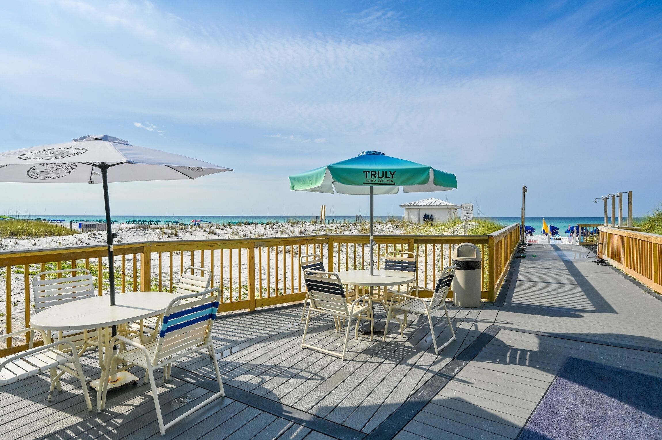 Eine Holzterrasse mit Sitzgelegenheiten und Sonnenschirmen mit Blick auf einen Strand.