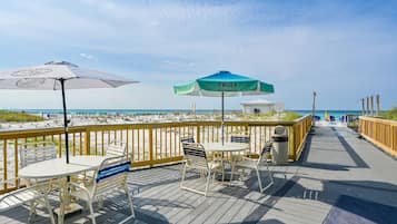 Eine Holzterrasse mit Sitzgelegenheiten und Sonnenschirmen mit Blick auf einen Strand.