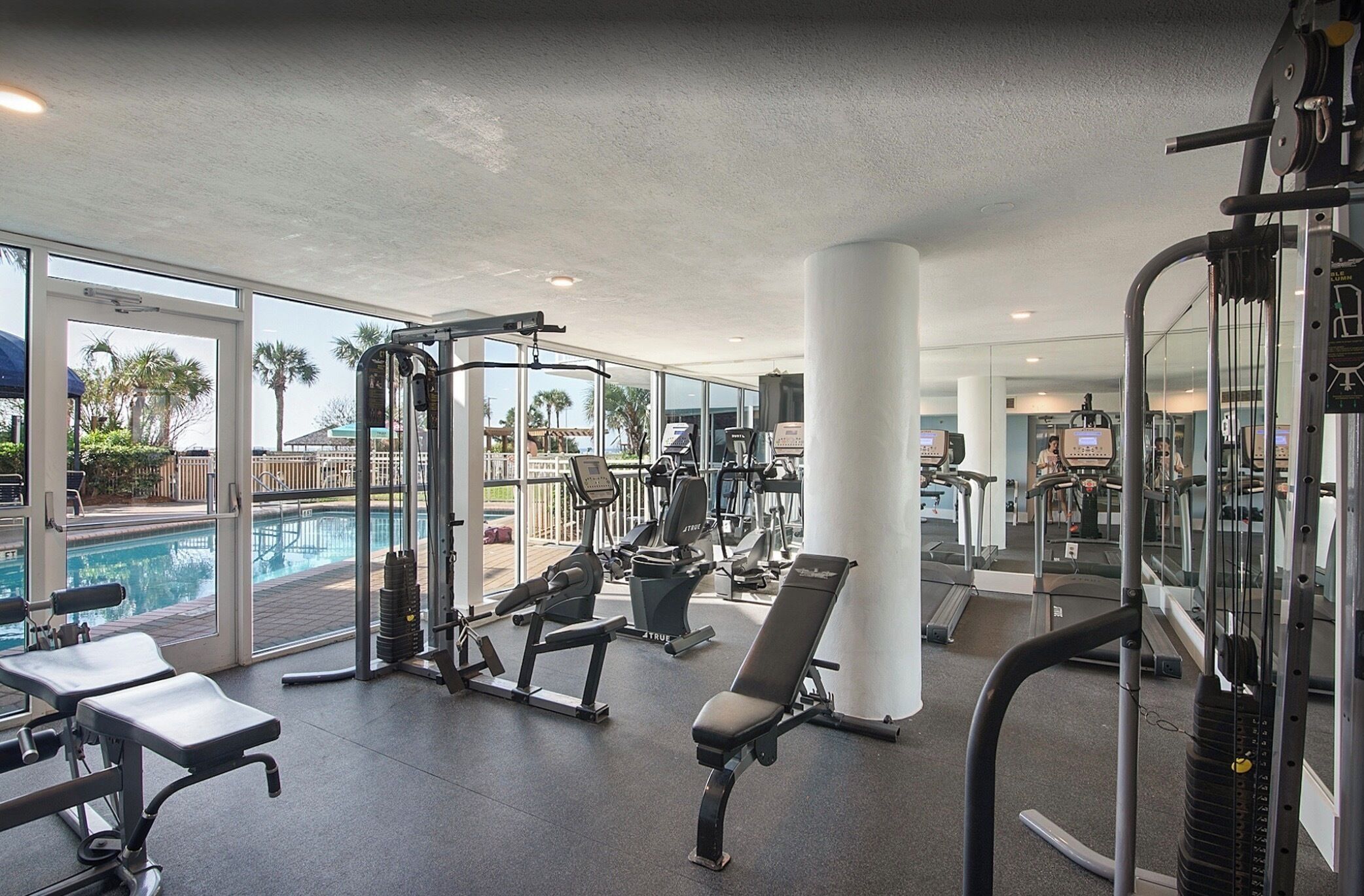 Une salle de sport équipée de matériel d’exercice, une piscine et de grandes fenêtres.