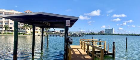 A wooden dock extending into calm water with a 'No Swimming Allowed' sign, surrounded by buildings and clear skies.