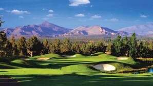 Un parcours de golf avec des collines verdoyantes, des bunkers de sable et, en toile de fond, des montagnes sous un ciel bleu dégagé.