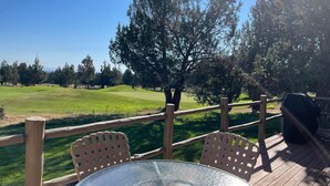 Une terrasse en bois avec une table et des chaises en verre, donnant sur un terrain de golf.