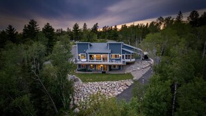 Una moderna casa a due piani con un'ampia terrazza, immersa in un paesaggio roccioso e una fitta foresta.