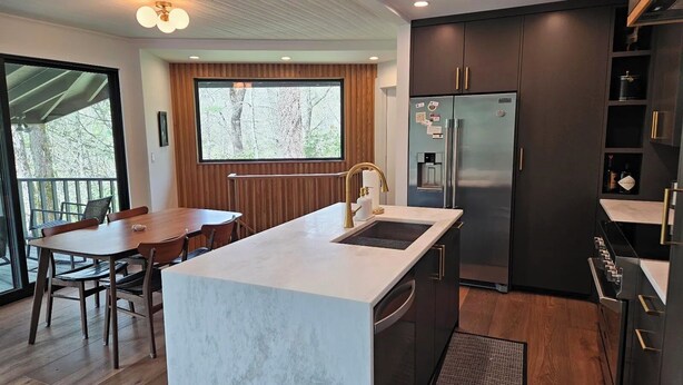 Una cocina moderna con una isla central, armarios oscuros y un ventanal grande.