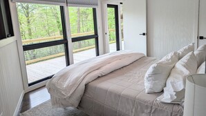 Un dormitorio con una cama grande, vista a una terraza de madera y una puerta corrediza que da a un espacio exterior.