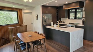 Una cocina moderna con una isla central, armarios oscuros y un comedor con mesa y sillas de madera.