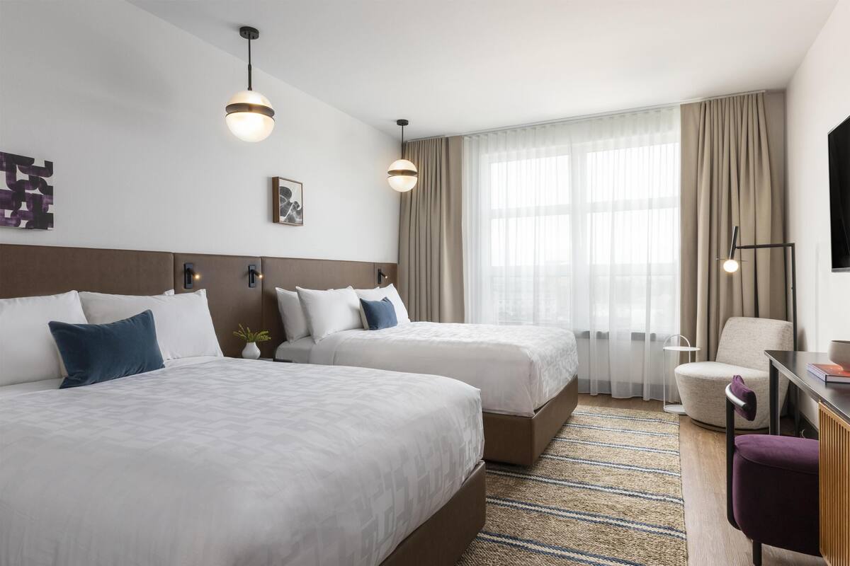 Une chambre d’hôtel avec deux lits, un bureau, une chaise et un téléviseur.