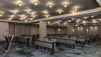Sala de conferencias con varias mesas y sillas, equipada con micrófonos y vasos.
