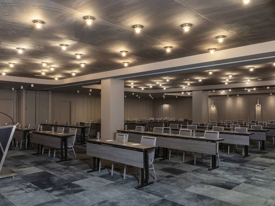 Sala de conferencias con varias mesas y sillas, equipada con micrófonos y vasos.
