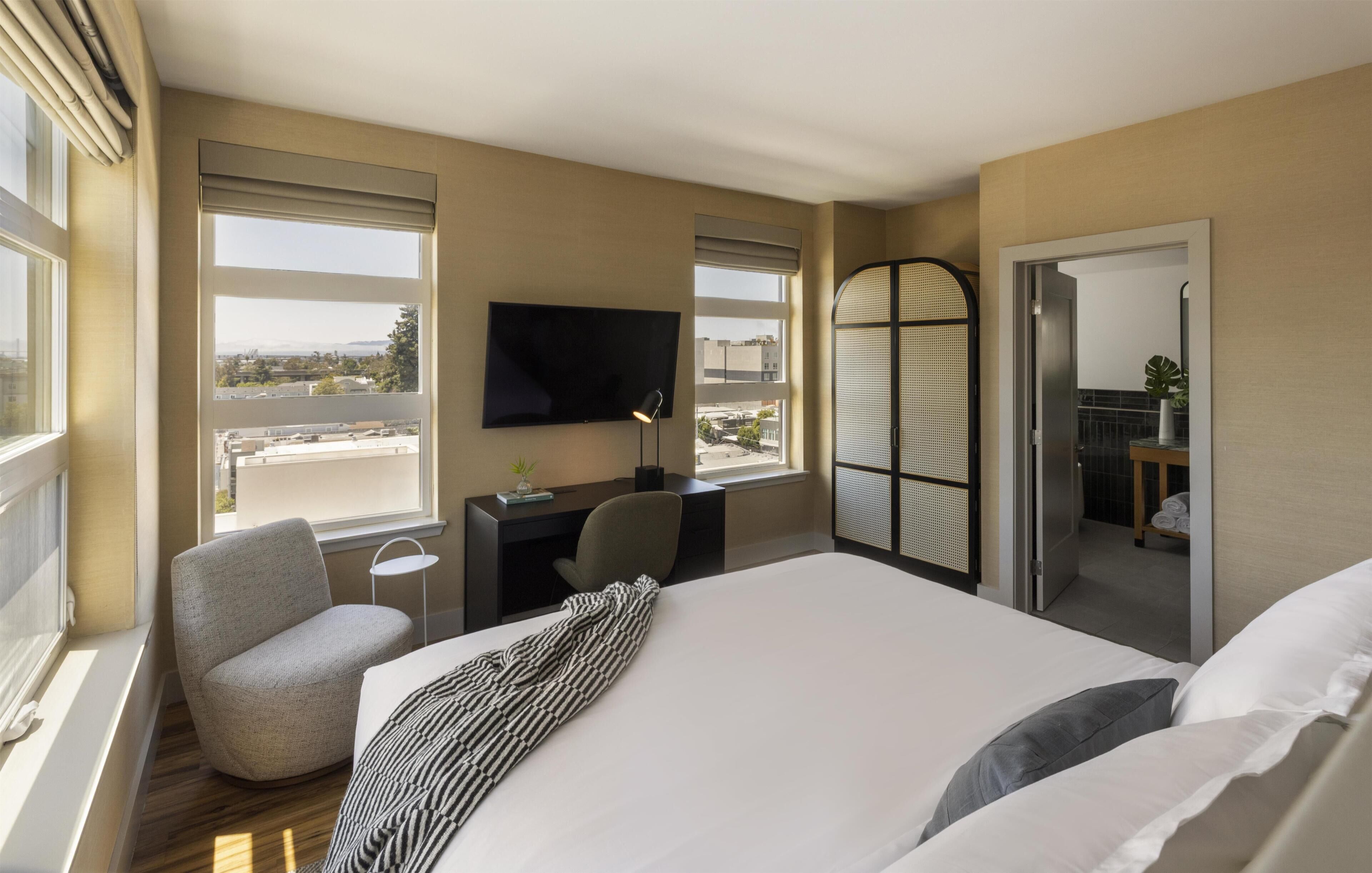 A hotel room with a large bed, a desk with a chair, a TV, and a balcony with a view.