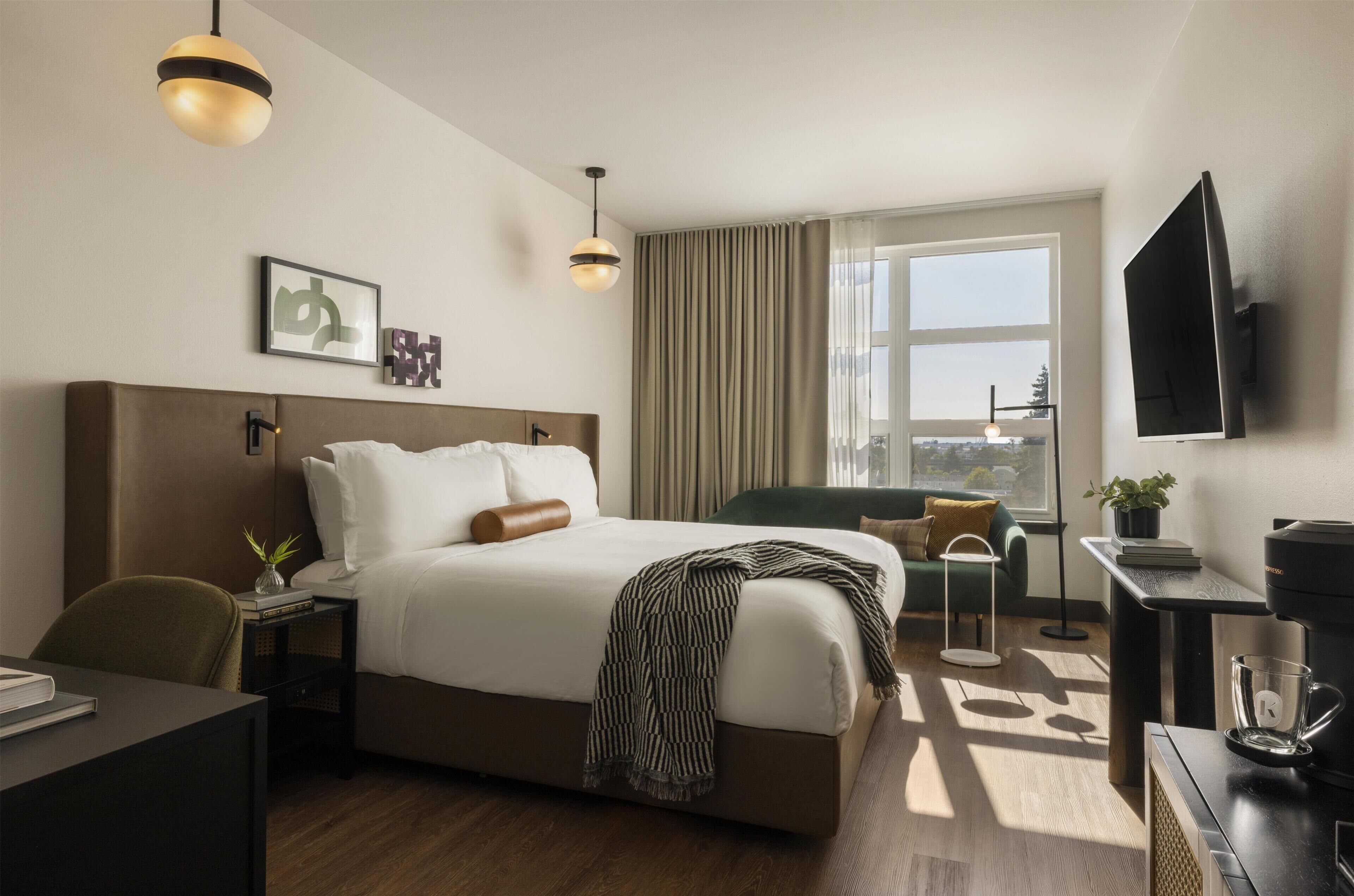 A hotel room with a large bed, a desk, a chair, a coffee maker, a TV, and a window with curtains.