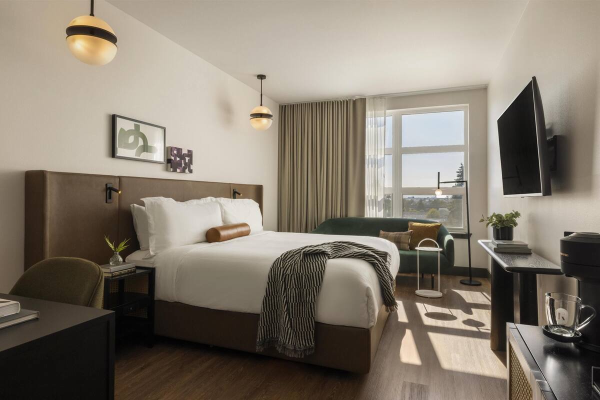 Une chambre d’hôtel avec un grand lit, un bureau, une chaise, une machine à café, une télévision et une fenêtre avec des rideaux.