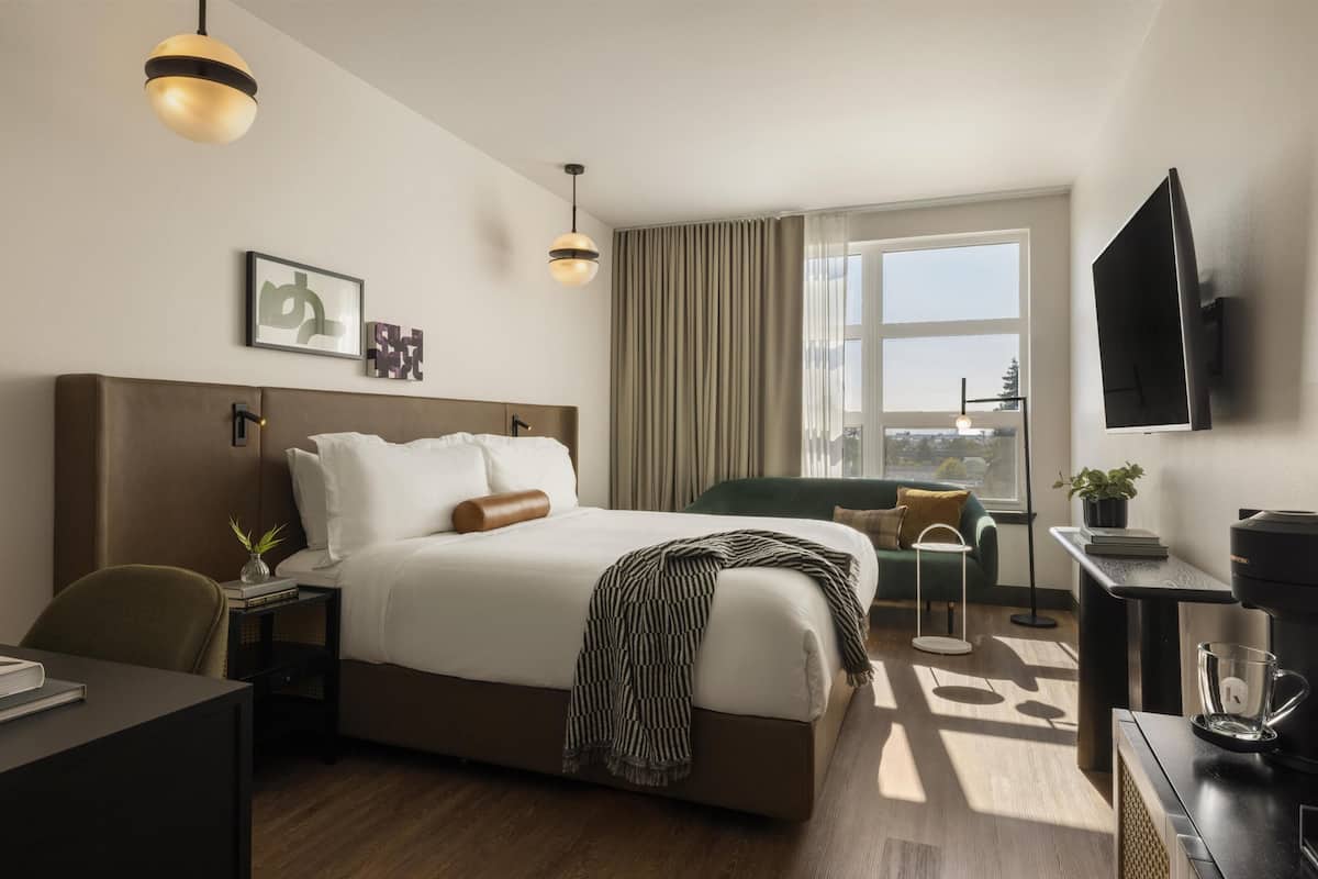 A hotel room with a large bed, a desk, a chair, a coffee maker, a TV, and a window with curtains.