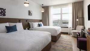 Une chambre d’hôtel avec deux lits, un bureau, une chaise, une télévision et une grande fenêtre avec des rideaux.