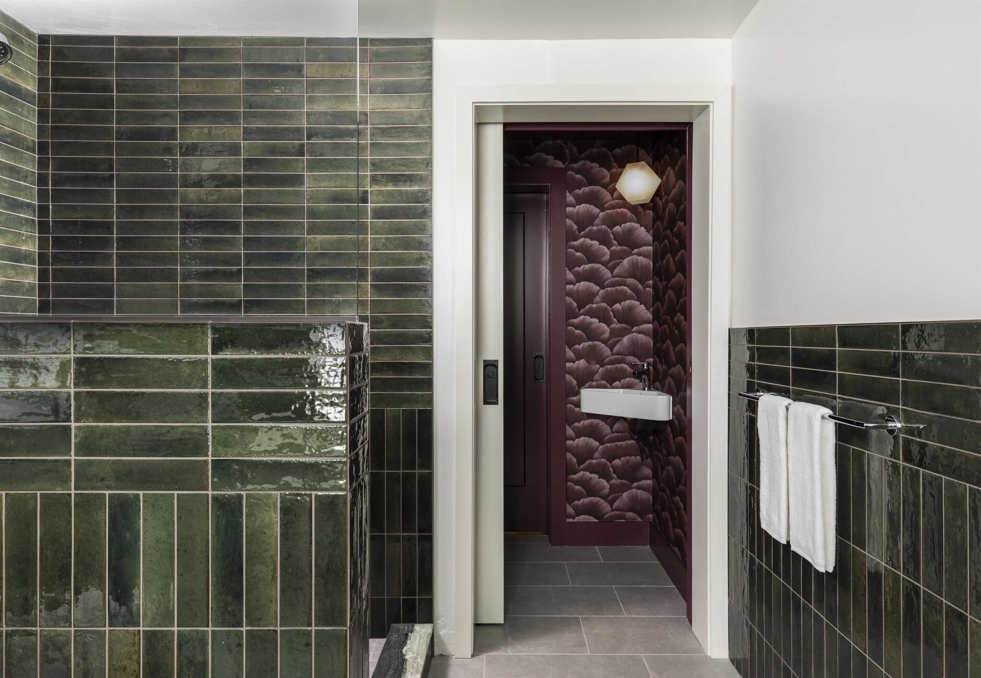 Un baño con azulejos verdes, una puerta oscura, un accesorio de iluminación y un perchero para toallas.