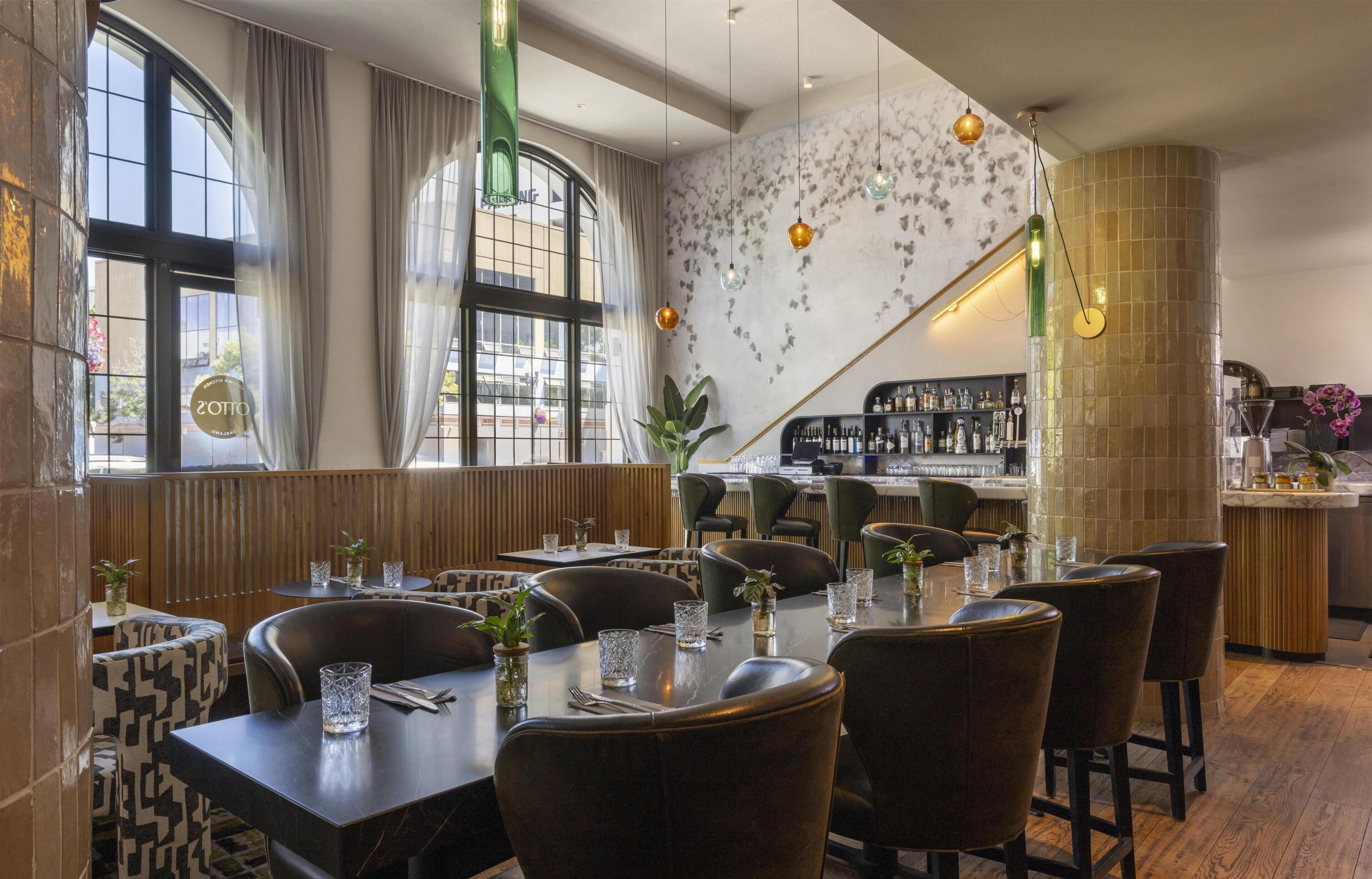 Interior de un restaurante con mesas preparadas para comer, una zona de bar y vistas a la calle.