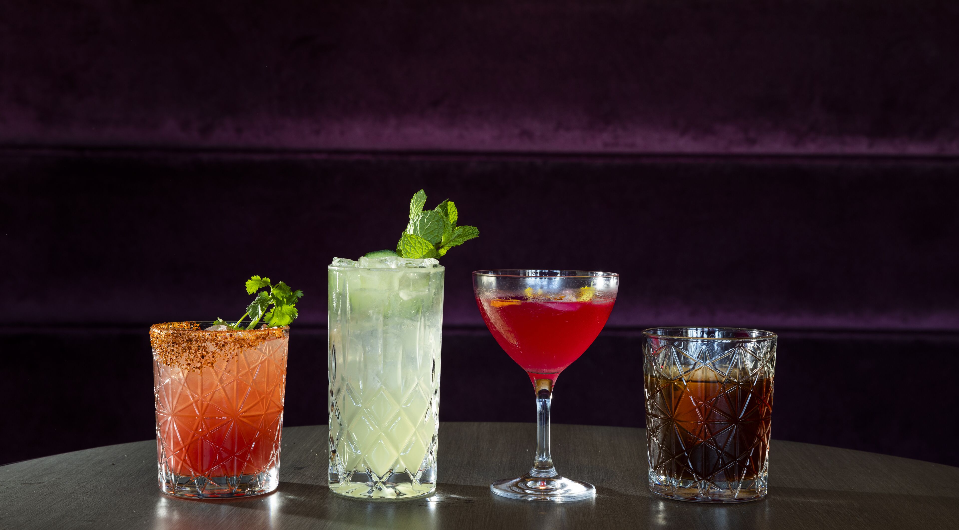 Four different cocktails in various glassware on a table against a dark background.