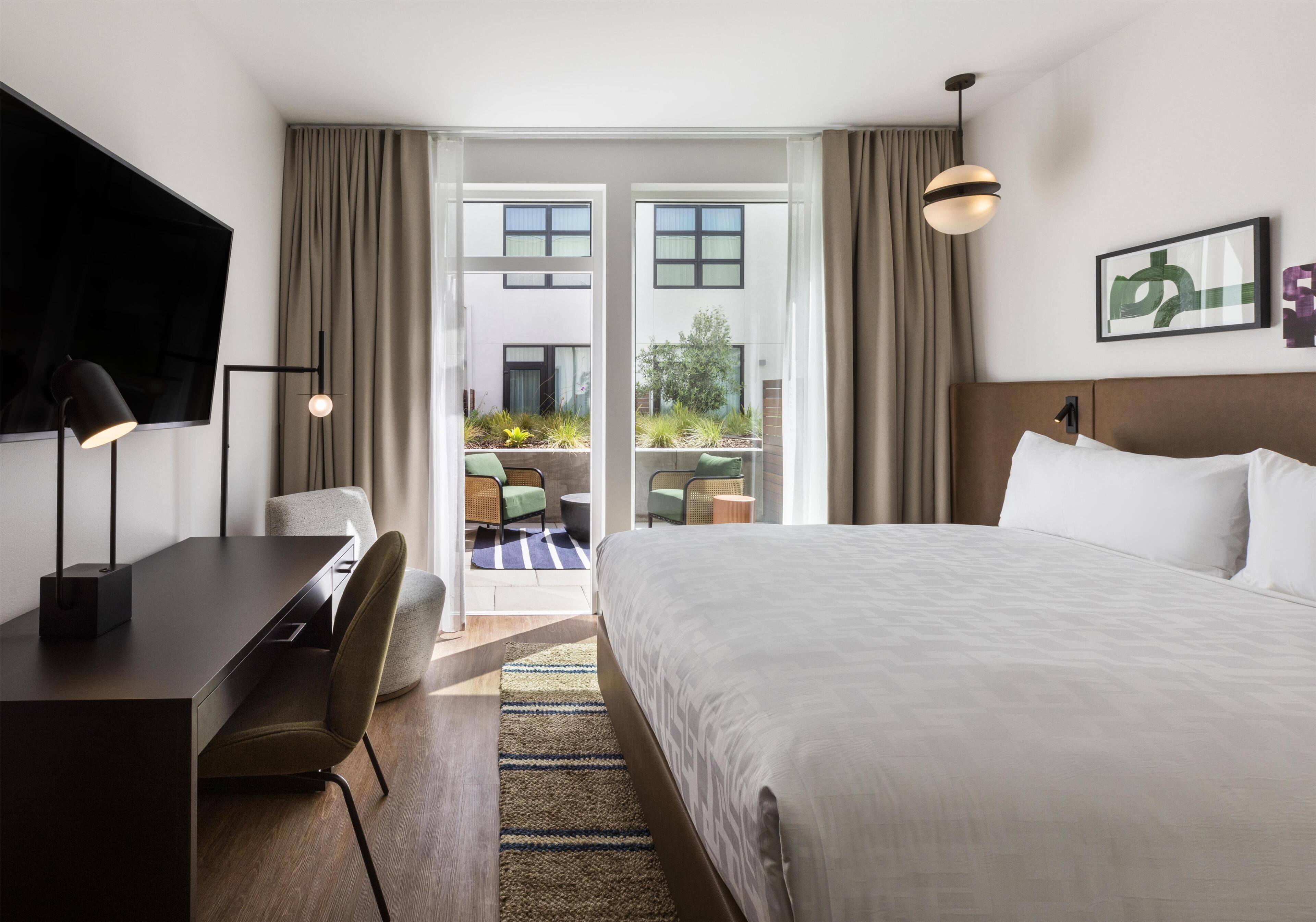 Una camera d'albergo con un letto, una scrivania, una sedia, televisore e vista esterna.