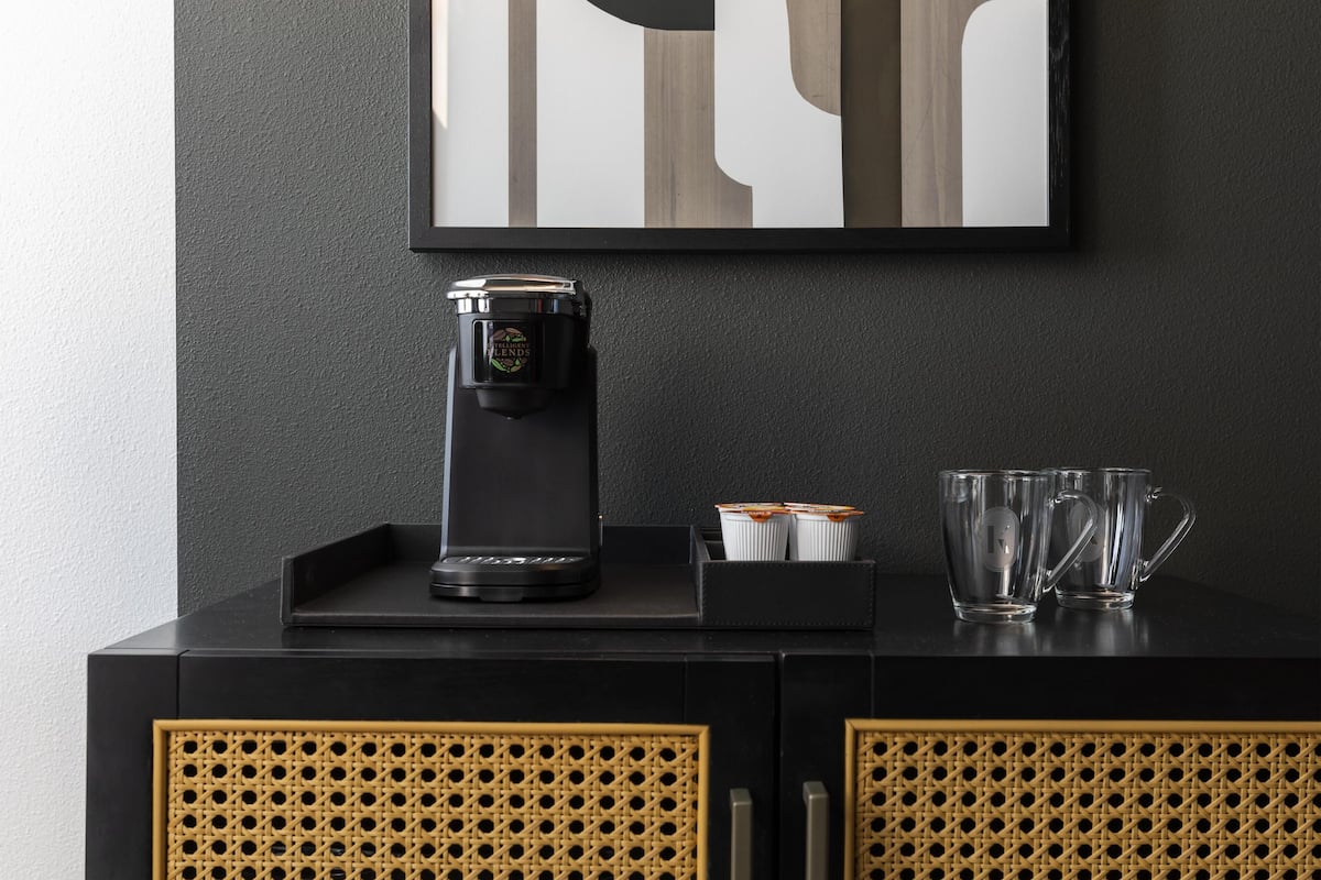 Una máquina de café negro sobre un mueble negro, con dos vasos y una bandeja.