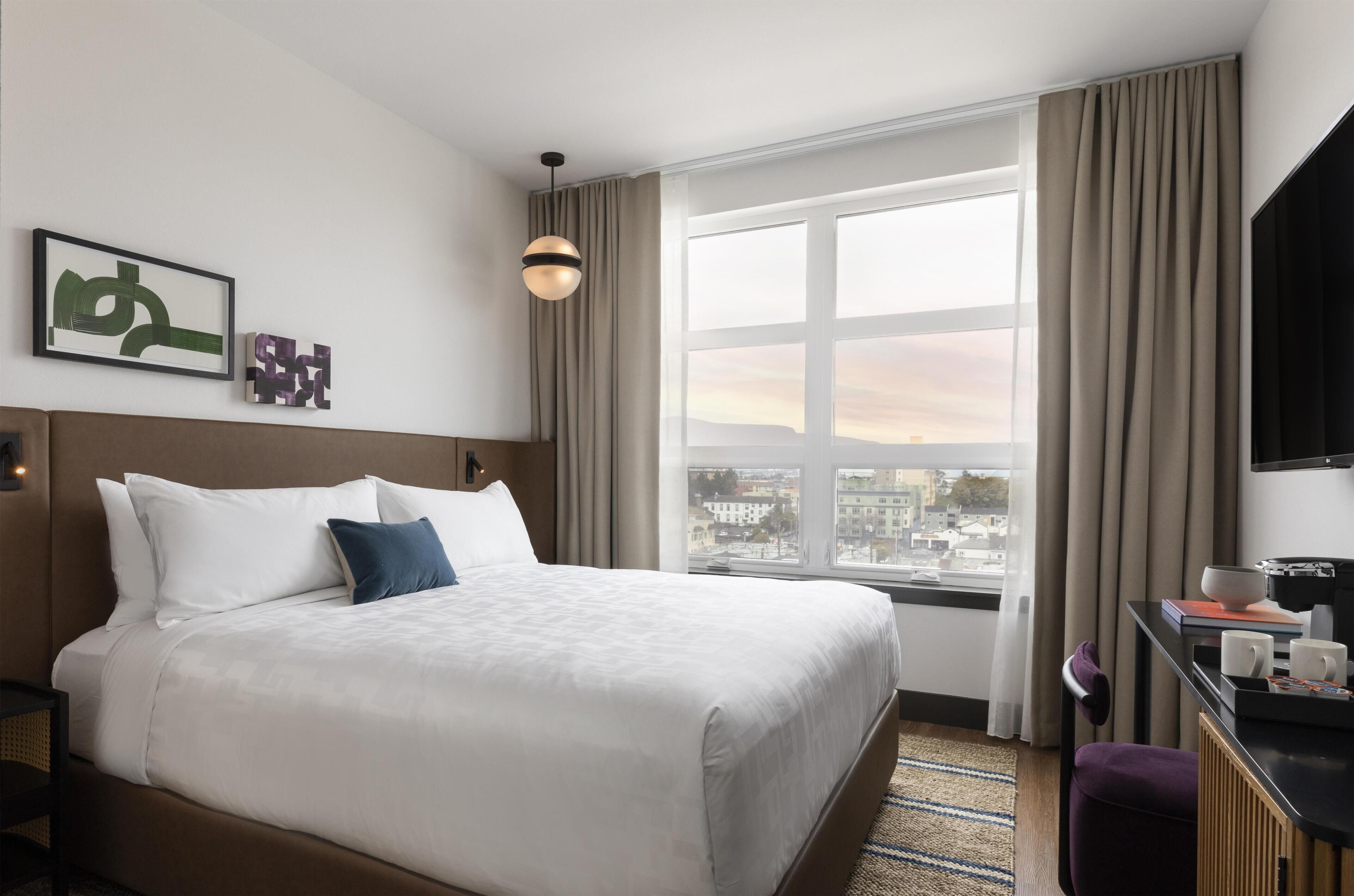 A hotel room with a large bed, a desk with a chair, a television, and a window with curtains.