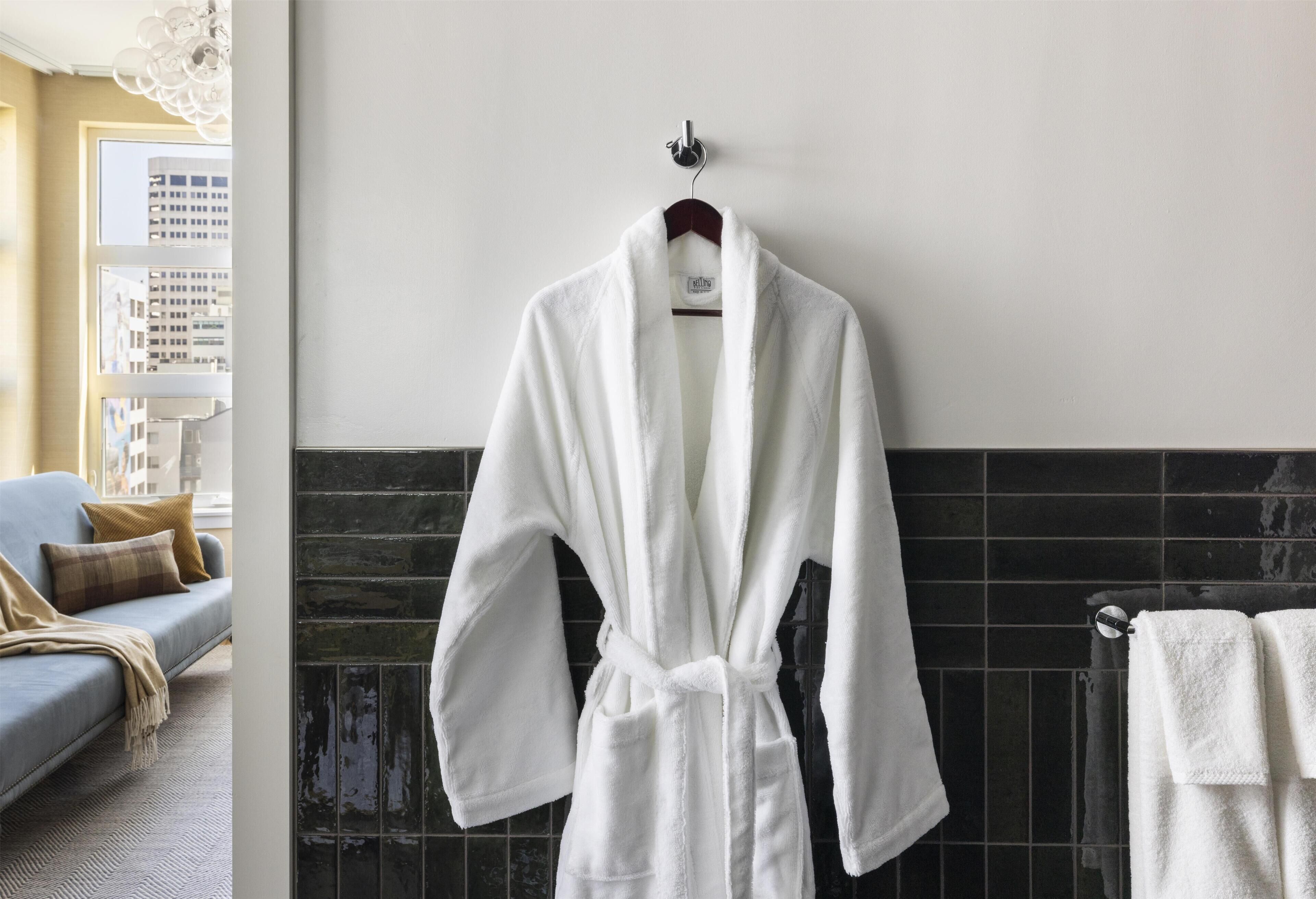 Un albornoz blanco colgado de un perchero en una habitación con un sofá gris y un revestimiento de azulejos.