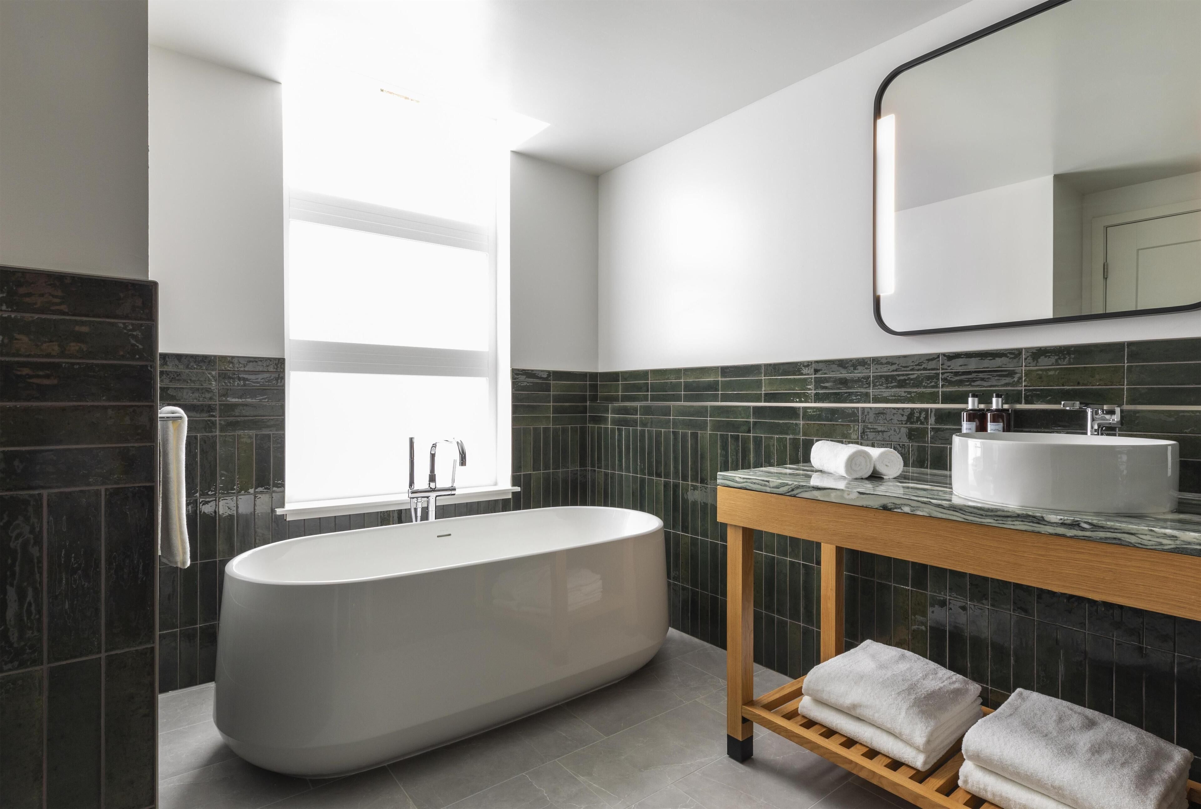 A modern bathroom with a freestanding bathtub, a wooden vanity, a large mirror, and a window providing natural light.
