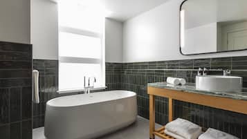 A modern bathroom with a freestanding bathtub, a wooden vanity, a large mirror, and a window providing natural light.