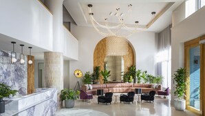Un hall d’entrée spacieux avec un comptoir de réception en marbre, un grand canapé en cuir, plusieurs fauteuils et un lustre moderne.