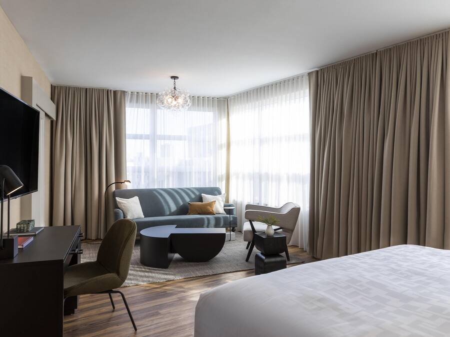 Quarto de hotel moderno com uma cama, um sofá, uma escrivaninha e uma televisão.
